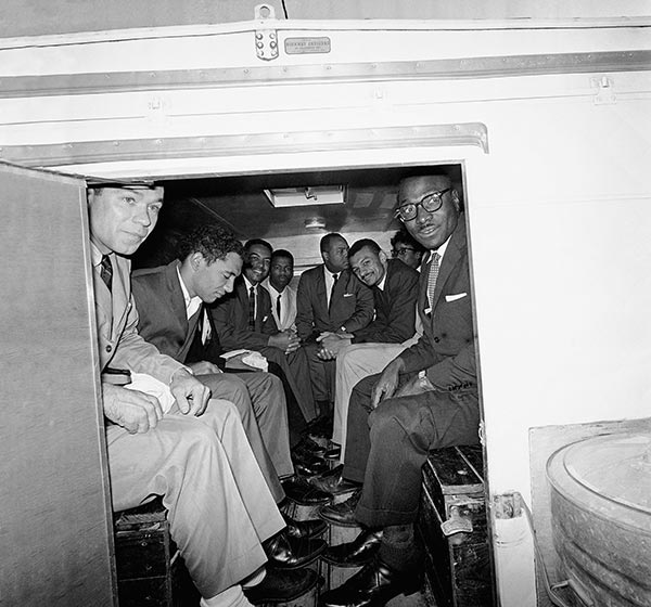 A black and white photograph of eight Freedom Riders sitting in a police wagon to be escorted to jail. Several are smiling at the camera. C.T. Vivian sits in center right. John Lewis is fourth from left.