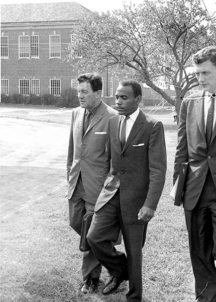 A black and white photograph of James Meredith, center, being escorted to class at the University of Mississippi by two white federal marshals.