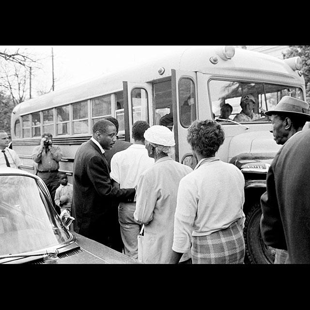Comedian Dick Gregory helping people onto a bus headed to the Greenwood courthouse to register to vote