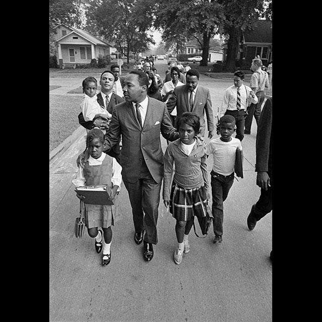 A black and white photograph of Dr. Martin Luther King Jr. walking with a group of students and adults in Grenada in 1966