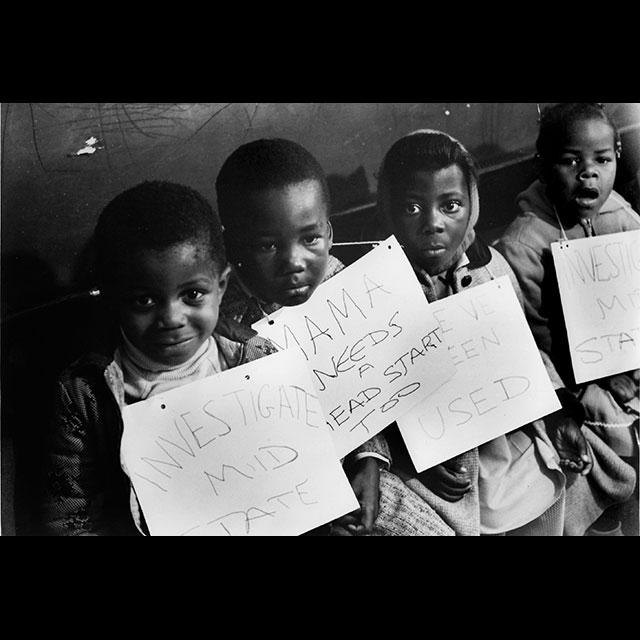 A black and white photograph of four students holding picket signs while traveling to Washington, D.C.